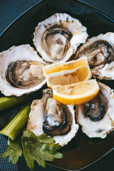 Fresh oysters with lemon and celery on a plate. Oyster season. Oyster on the half shell.