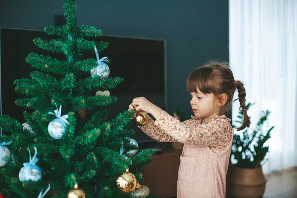 stock image Cute little girl hanging ornaments and balls on Christmas tree. Kid decorating Christmas tree.