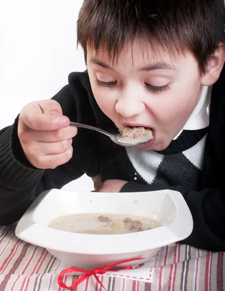 Мальчик ест суп с фрикадельками — стоковое фото