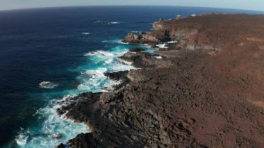 Kara kahverengi lavlardan oluşan kayalık bir sahil kulesi ve kanarya Adaları 'ndaki El Hierro adasının Verodal plajı yakınlarındaki güneşsiz havada okyanus dalgası sörfü.