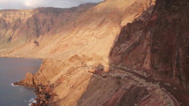 Havadan çekilen doli solda, kaldera Las Playas 'ın arkası sabah güneşi altında kısmi bulut gölgesi altında, Atlas Okyanusu' nun karşısından Roque de La Bonanza 'ya yakın eski yoldan sahile doğru çekiliyor.