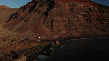 Atlas Okyanusu kıyısındaki hava aracı, İspanya 'nın Kanarya Adaları' ndaki El Hierro Adası 'ndaki kayalık volkanik dağların zemininde bordo kırmızı kumla Verodal sahiline doğru yaklaşıyor.