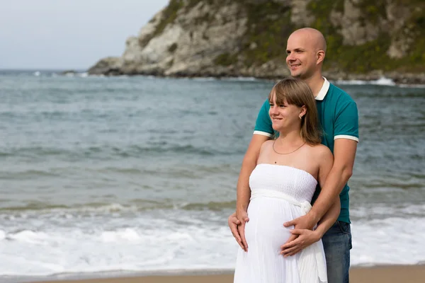 Zwangere vrouw en haar echtgenoot wandeling door de zee. — Stockfoto