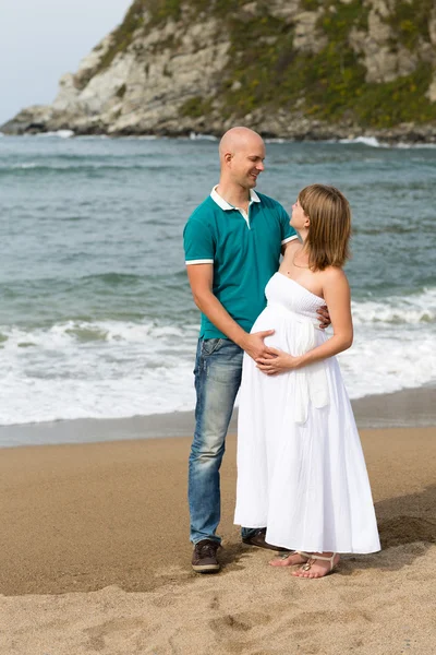 Pregnant woman and her husband strolling by the sea. Stock Image