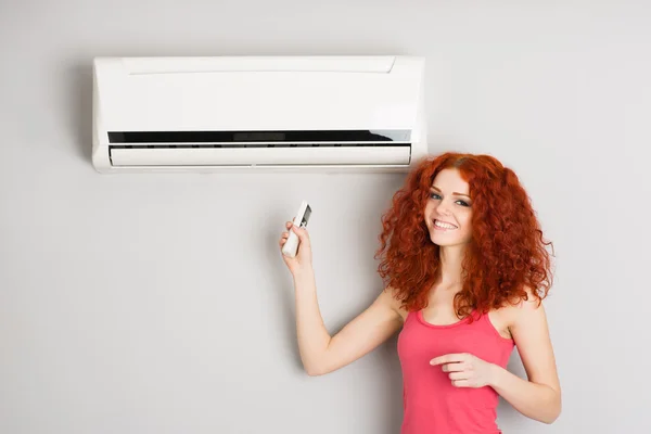 Red haired meisje houden een afstandsbediening airconditioner — Stockfoto