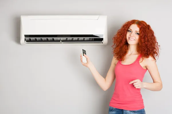 Smiling redhead girl holding a remote control air conditioner — Stock Photo, Image