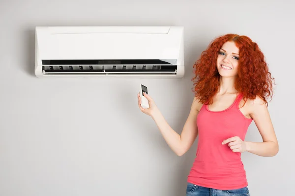 Lachende roodharige meisje houden een afstandsbediening airconditioner Rechtenvrije Stockfoto's