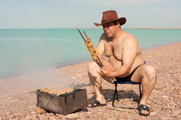 Der erwachsene Mann bereitet gebratenes Fleisch zu. auf dem See. Ruhe. Stockbild