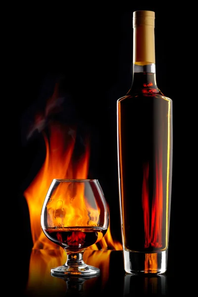 Flasche und Glas Cognac auf dunklem Hintergrund mit Flamme — Stockfoto