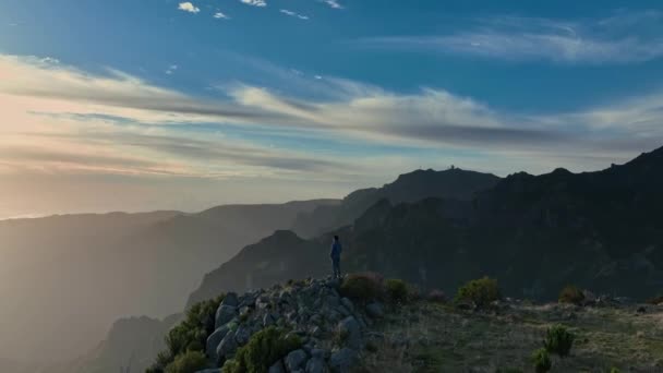 Dağlardaki tırmanışçı amacına ulaştı ve harika doğanın tadını çıkarıyor. Madeira adasının dağlarındaki muhteşem gün doğumunun havadan görüntüsü. İnsan dağın tepesinde durur ve güneşin doğuşunu seyreder. — Stok video