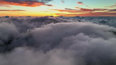 Gorgeous sunset above the clouds. Aerial shot of dense veil of clouds and bright red sunset sky. Flying above clouds.