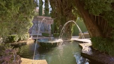 Slow motion gimbal shot of fountain surrounded by trees in Gardens of the Generalife in Alhambra. Granada, Spain.