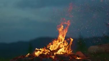 Gün batımında kamp ateşi dağların ve ormanın arka planına karşı. Havada kıvılcımlar uçuşan turist şenlik ateşi, yavaş çekim.