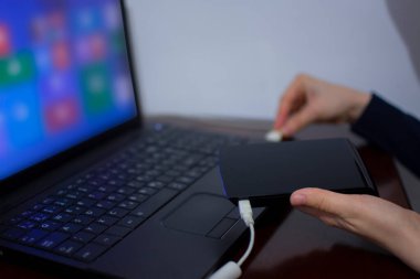 Bilgisayara kablo bağlarken harici sabit diski tutan kadın. Corona virüsü salgını yüzünden evden çalışıyor. Covid 19 ve çevrimiçi öğrenme. Yeni yaşam tarzı