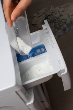 Çamaşır makinesine çamaşır deterjanı döken kadın elini kapat.