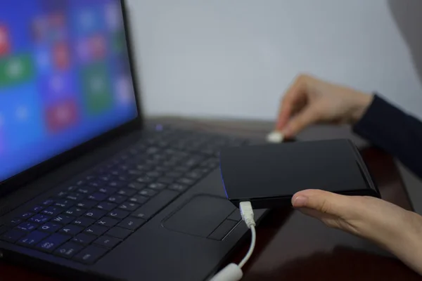 Woman holding external hard drive while plugging cable in the laptop