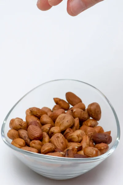 Hazel or hazelnuts in a glass bowl isolated on white background and the little part of the female hand — Stock Photo, Image