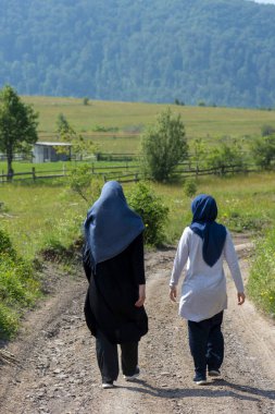 Kırsal dağ yolunda önlerinde güzel manzarayla yürüyen iki müslüman kız. Doğada tesettürlü kadınlar İslam dinini temsil eder.