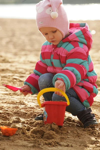 Little girl playing with sand at the autumn beach Royalty Free Stock Images