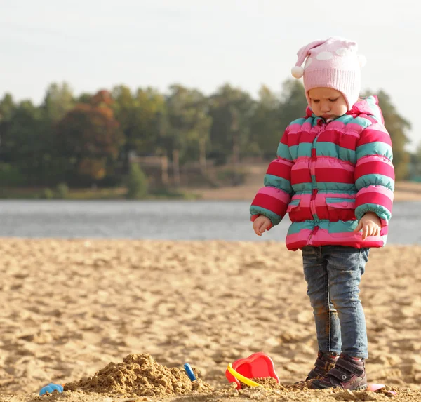 Little girl playing with sand at the autumn beach — Stock Photo, Image