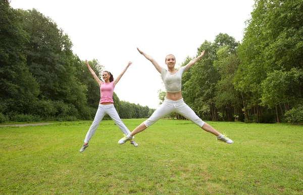 Две молодые девушки прыгают в летнем парке . — стоковое фото