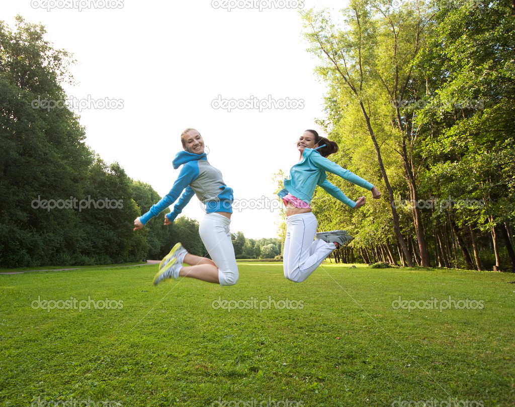 Two young girls jump in summer park.