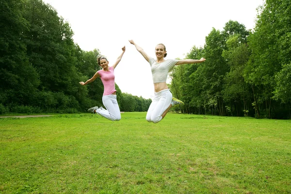 Two young girls jump in summer park. — Stock Photo, Image