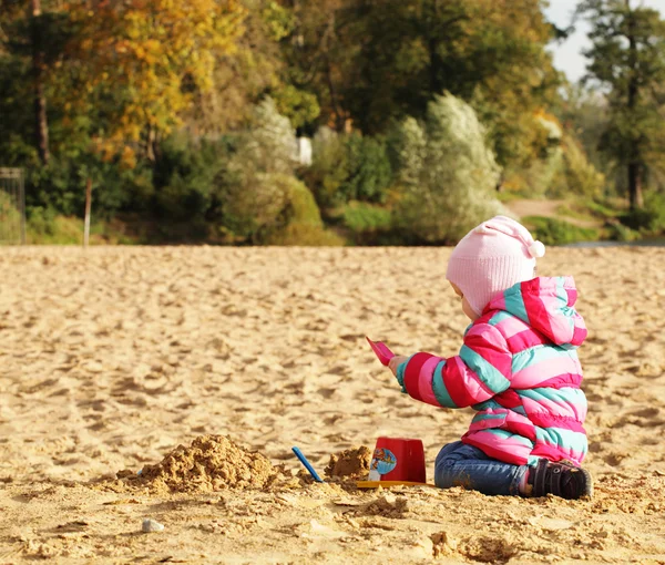 Kleines Mädchen spielt mit Sand am Herbststrand — Stockfoto