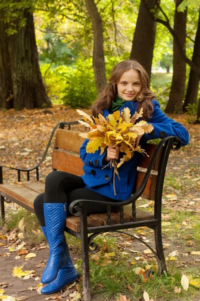 Junge Frau mit Herbstblättern sitzt auf Bank — Stockfoto