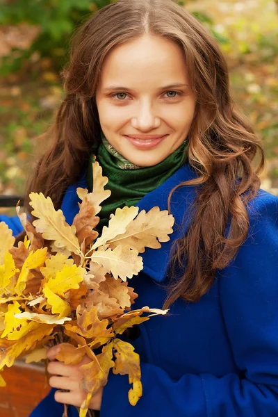 Jeune femme avec des feuilles d'automne assis sur le banc — Photo
