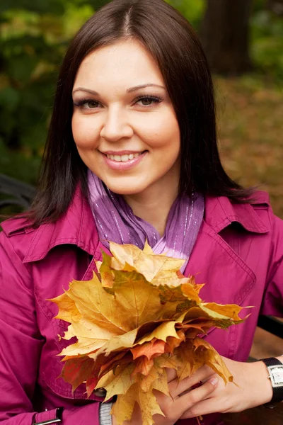 Mujer elegante con hojas de otoño sentado en el banco —  Fotos de Stock