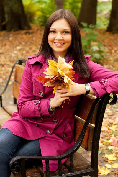 Žena s podzimními listy sedí na lavičce — Stock fotografie