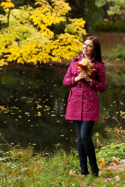 Giovane donna con foglie autunnali nel parco — Foto Stock