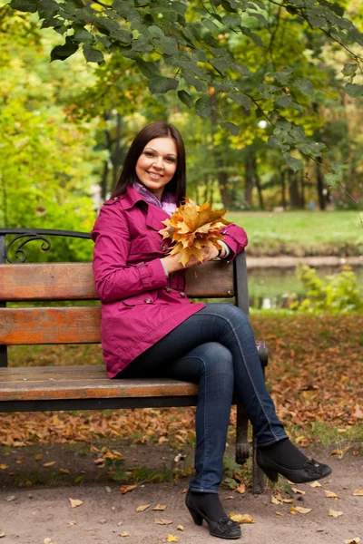 Jeune femme avec des feuilles d'automne assis sur le banc — Photo