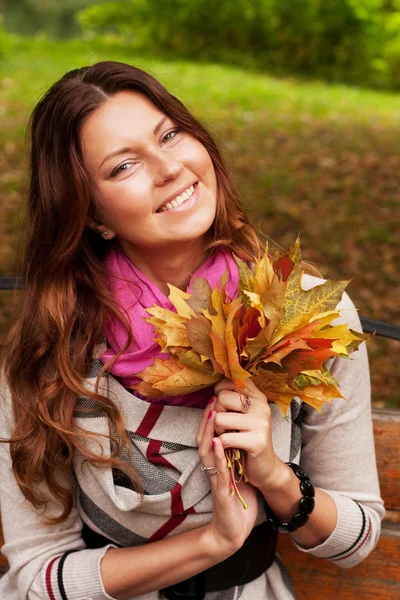 Mujer con hojas de otoño sentada en el banco —  Fotos de Stock