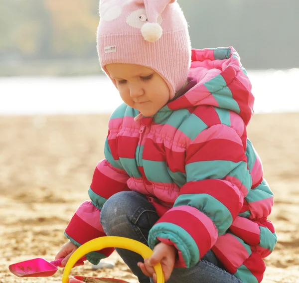 Lille pige leger med sand på efterårsstranden - Stock-foto