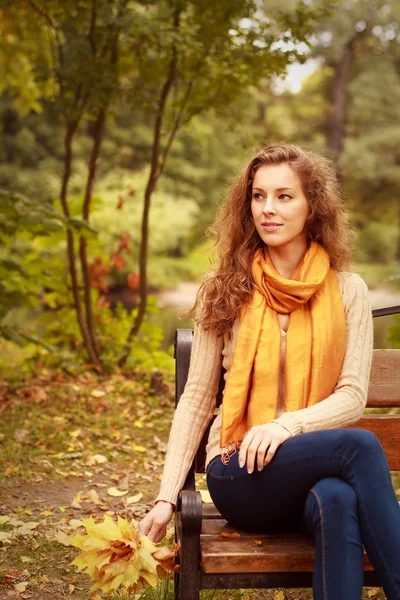 Vrouw met herfstbladeren zittend op bank — Stockfoto