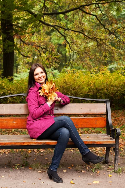 Žena s podzimními listy sedí na lavičce — Stock fotografie