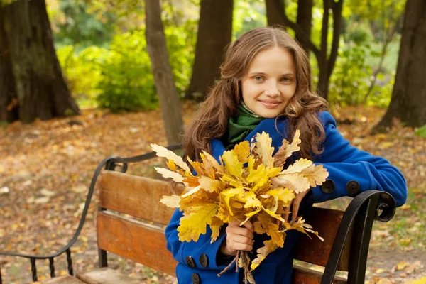 Žena s podzimními listy sedí na lavičce — Stock fotografie