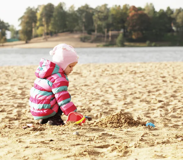 Little girl playing with sand at the autumn beach — Stock Photo, Image