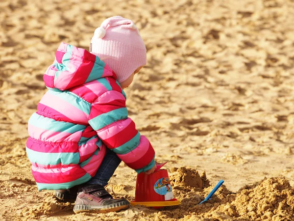 Little girl playing with sand at the autumn beach — Stock Photo, Image