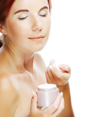 Genç gülümseyen kadın yüzüne krem sürüyor.