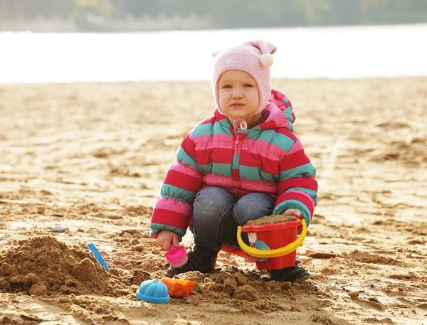 Little girl playing with sand at the autumn beach — Stock Photo, Image
