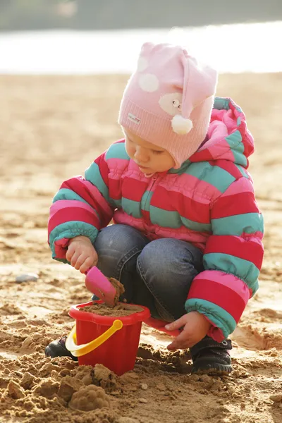 Little girl playing with sand at the autumn beach — Stock Photo, Image