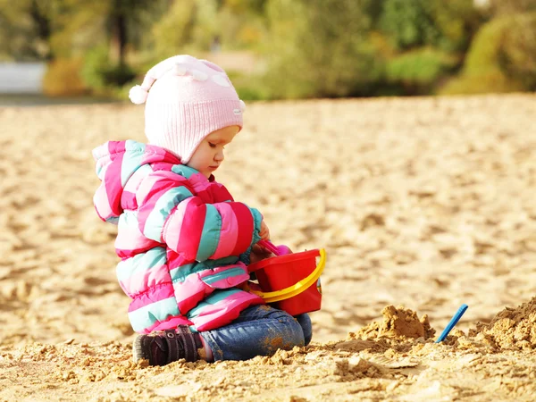 Little girl playing with sand at the autumn beach — Stock Photo, Image