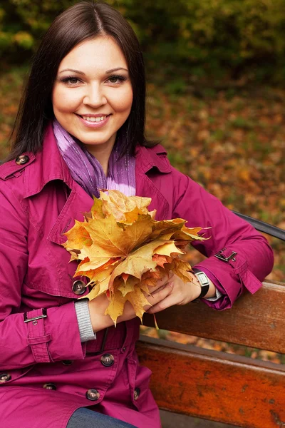 Mujer con hojas de otoño sentada en el banco — Foto de Stock