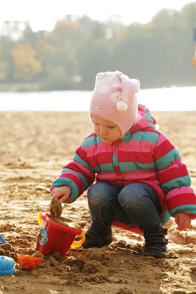 Kum ile sonbahar sahilde oynarken küçük kız. — Stok fotoğraf