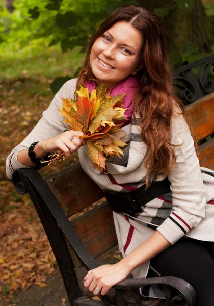 Elegante donna con foglie autunnali seduta su panchina — Foto Stock