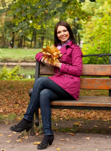 Jeune femme avec des feuilles d'automne assis sur le banc — Photo