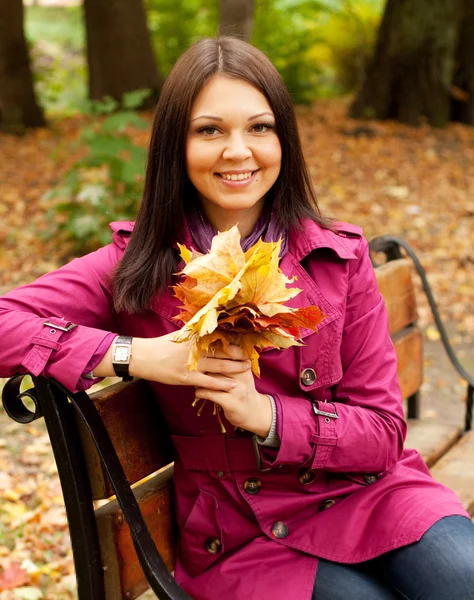벤치에 앉아 있는 가을 나뭇잎을 가진 여성 — 스톡 사진